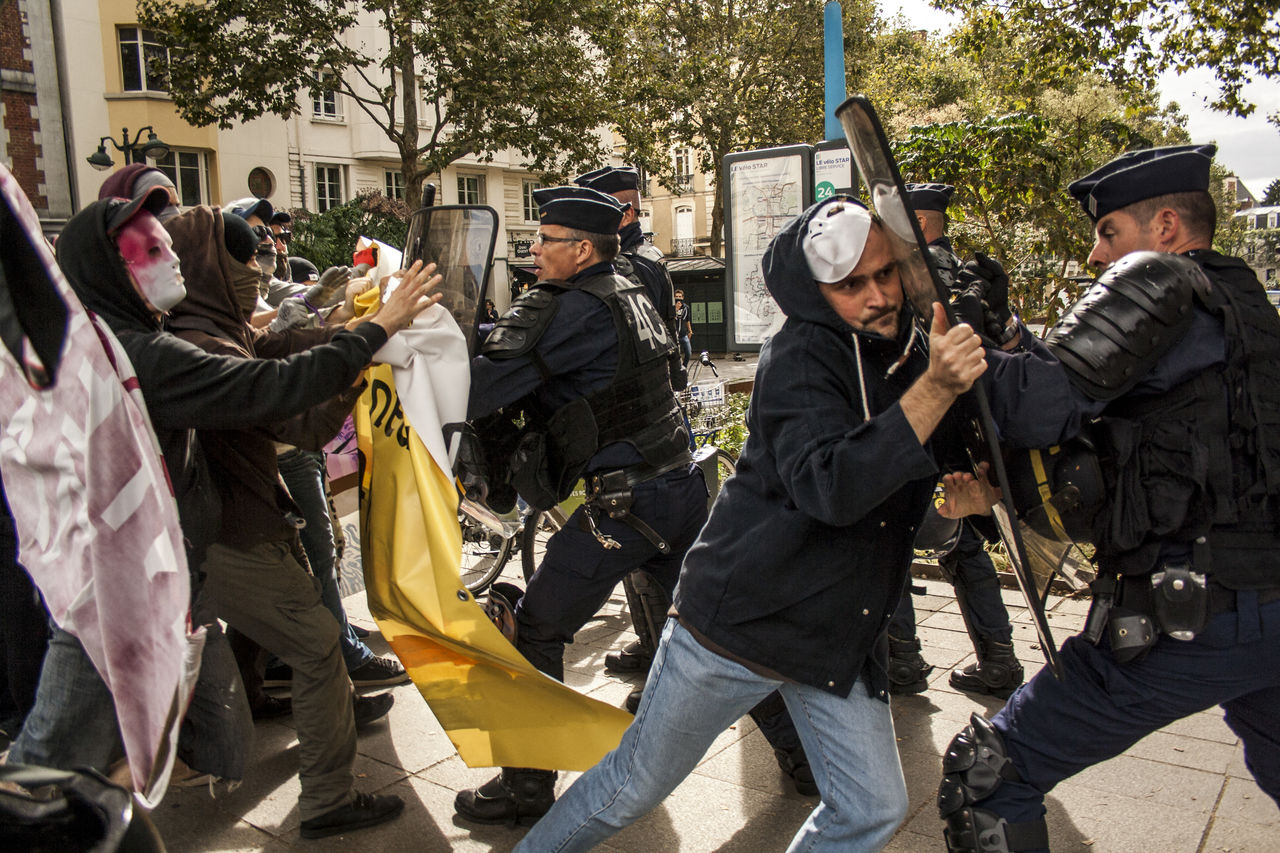 group of people, law, marching, protest, government, police force, men, person, weapon, troop, clothing, day, outdoors, adult, violence, architecture, security