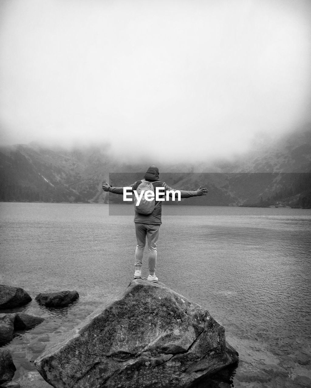 Rear view of man standing on rock by lake