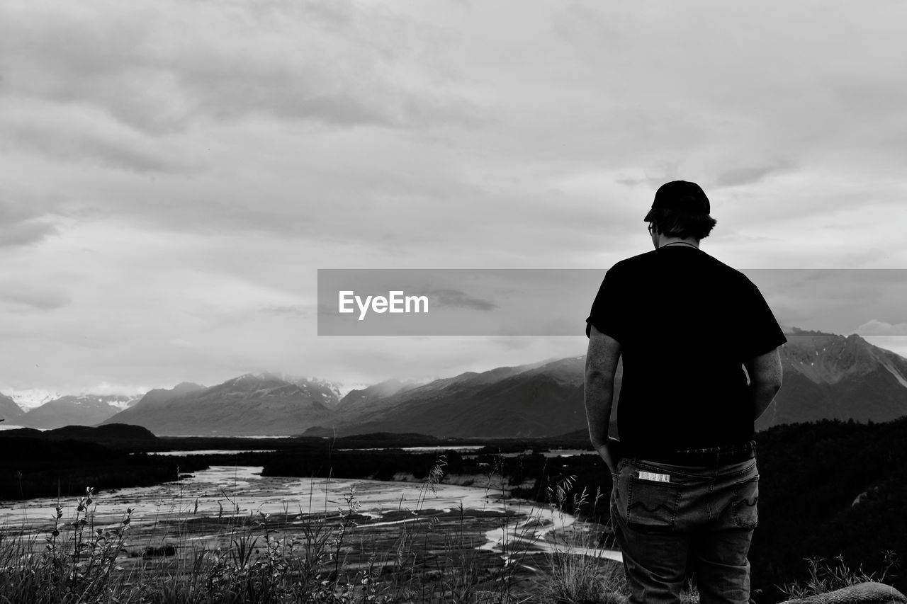 REAR VIEW OF MAN STANDING ON MOUNTAIN