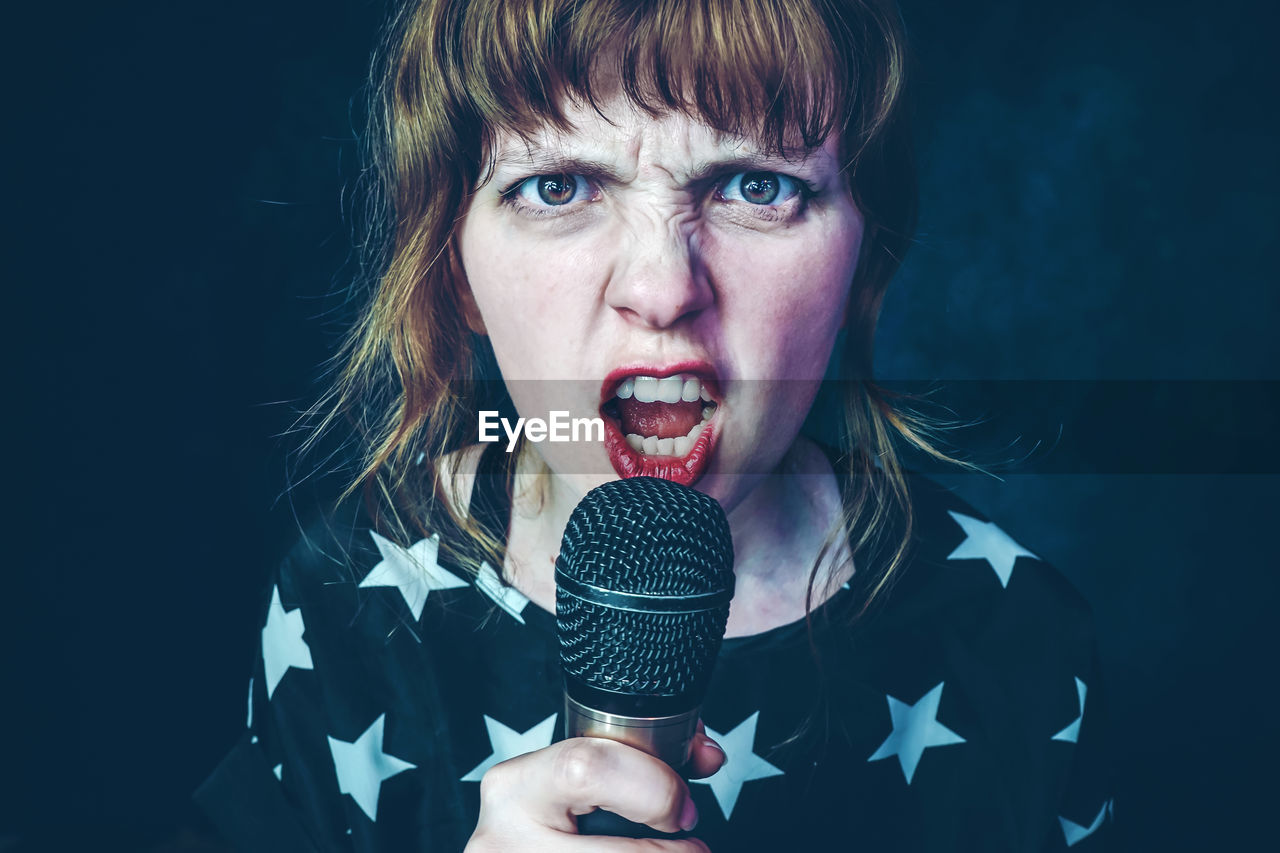 Portrait of mid adult woman singing while standing against black background