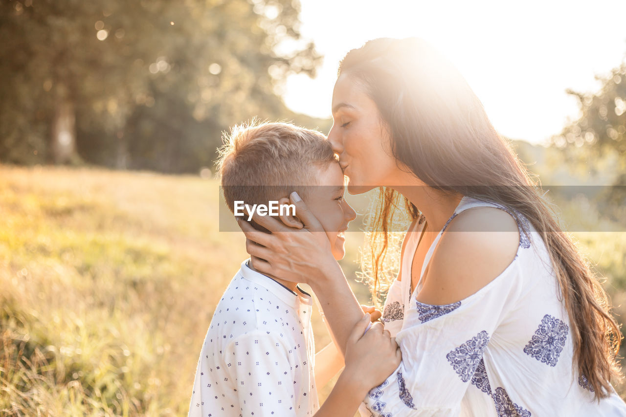 Mother kissing on son forehead in sunny day