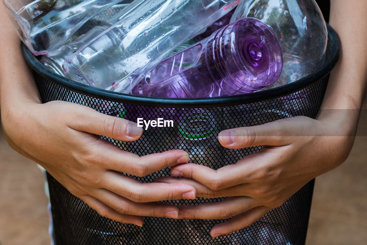 Midsection of woman holding garbage can of bottles