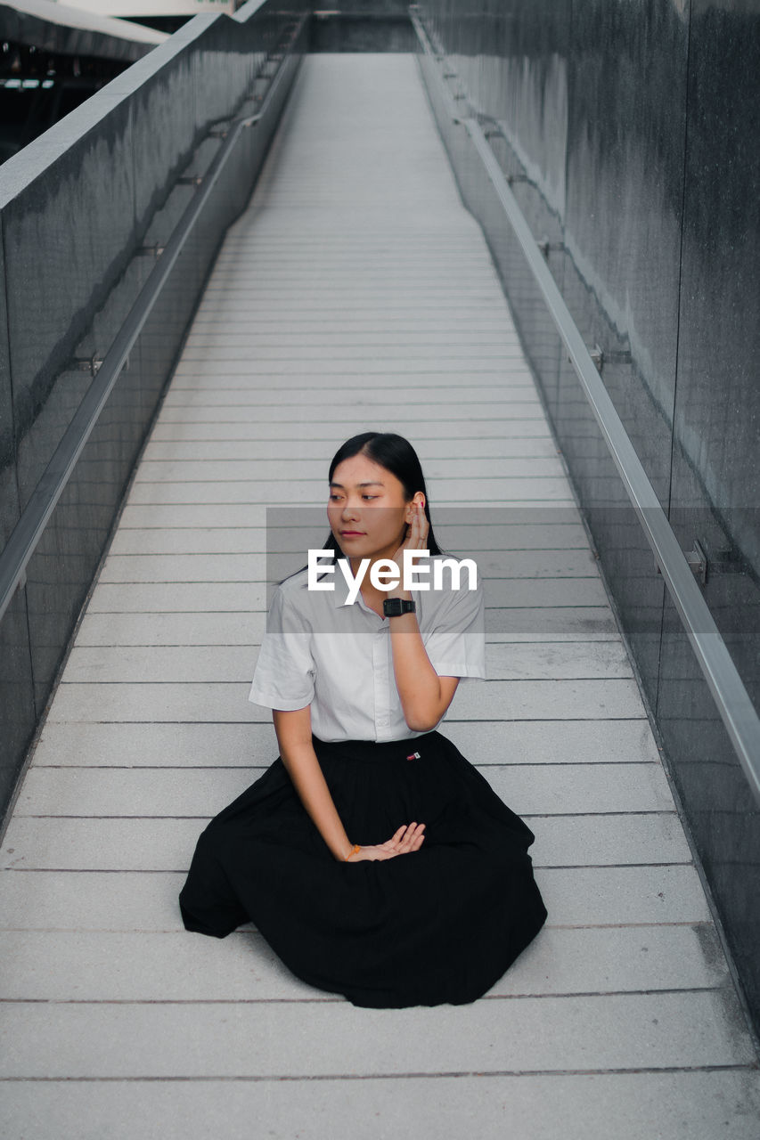 High angle view of woman looking away while sitting on walkway