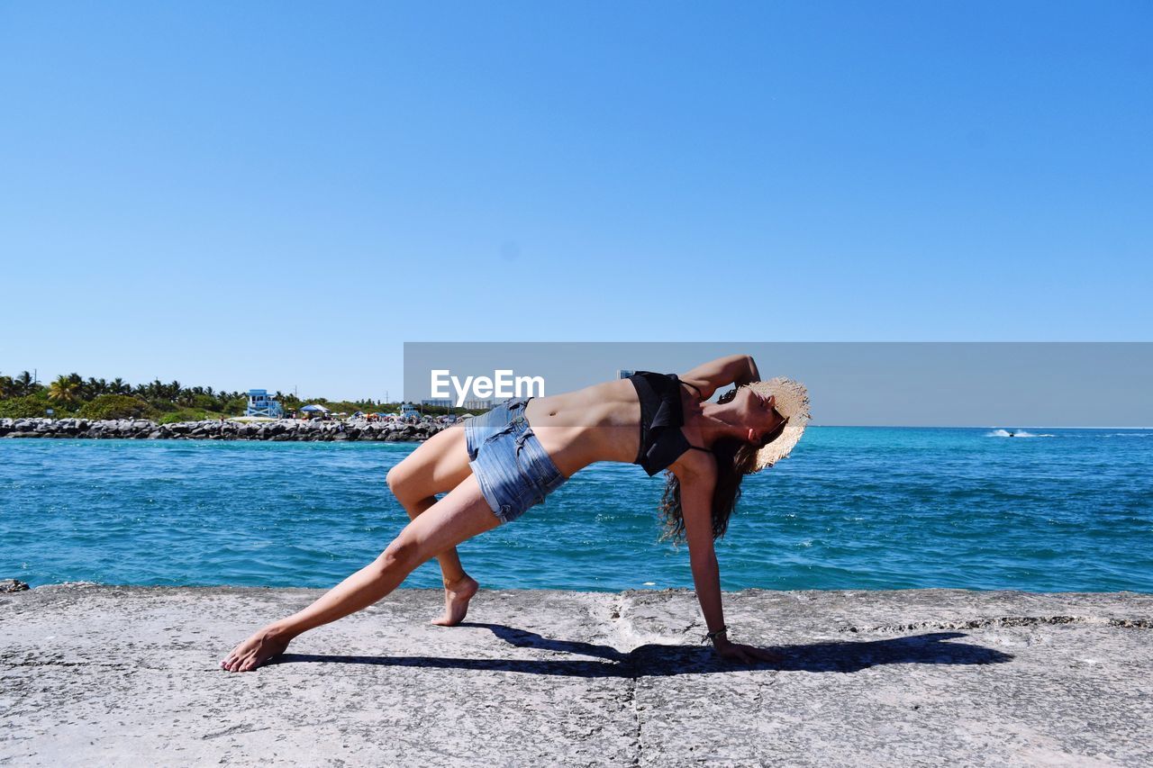 Woman exercising at beach against clear sky