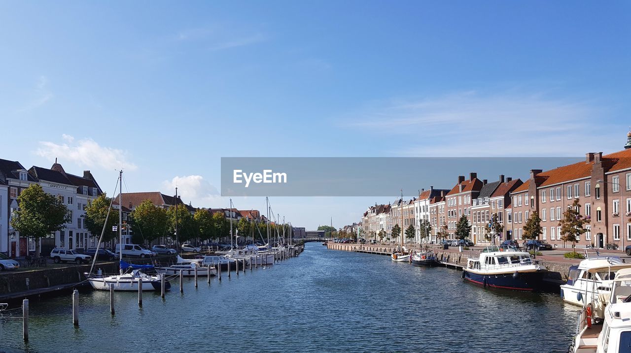 Sailboats moored on canal amidst buildings in city against sky