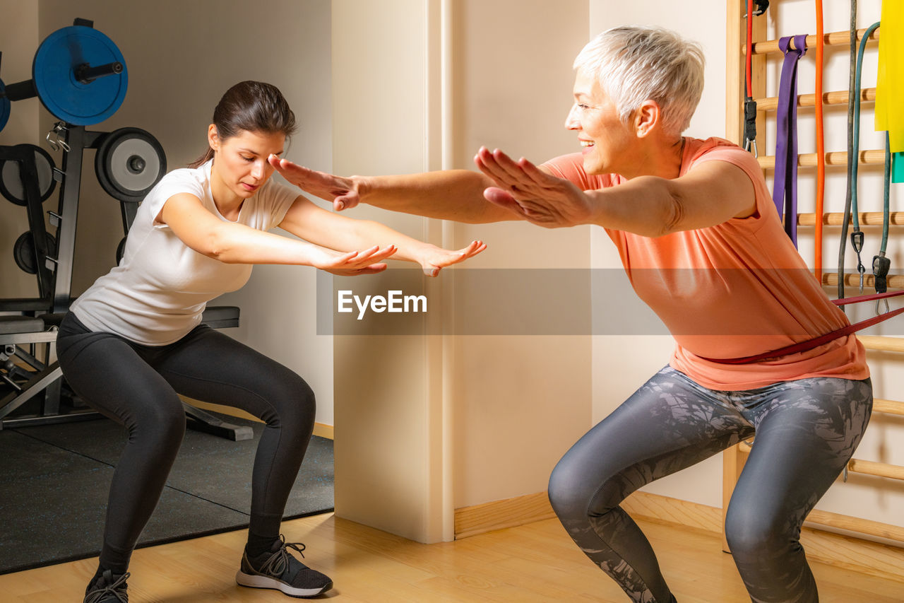 Female fitness instructor instructing mature woman exercising in gym