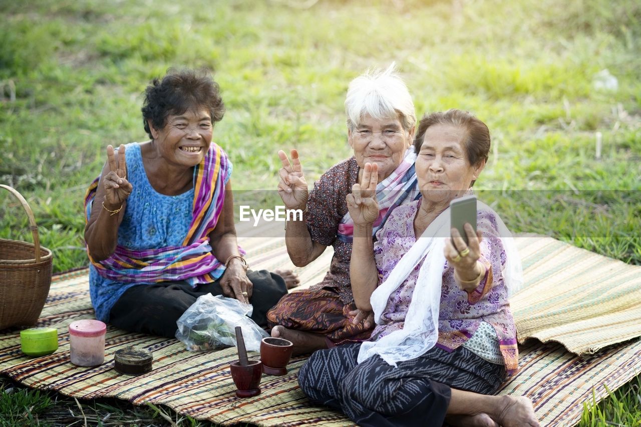 Senior women taking selfie while sitting on picnic blanket