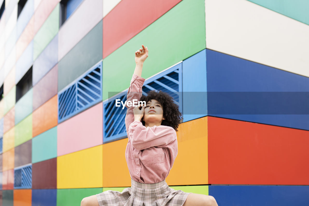 Female dancer with hand raised in front of colorful building