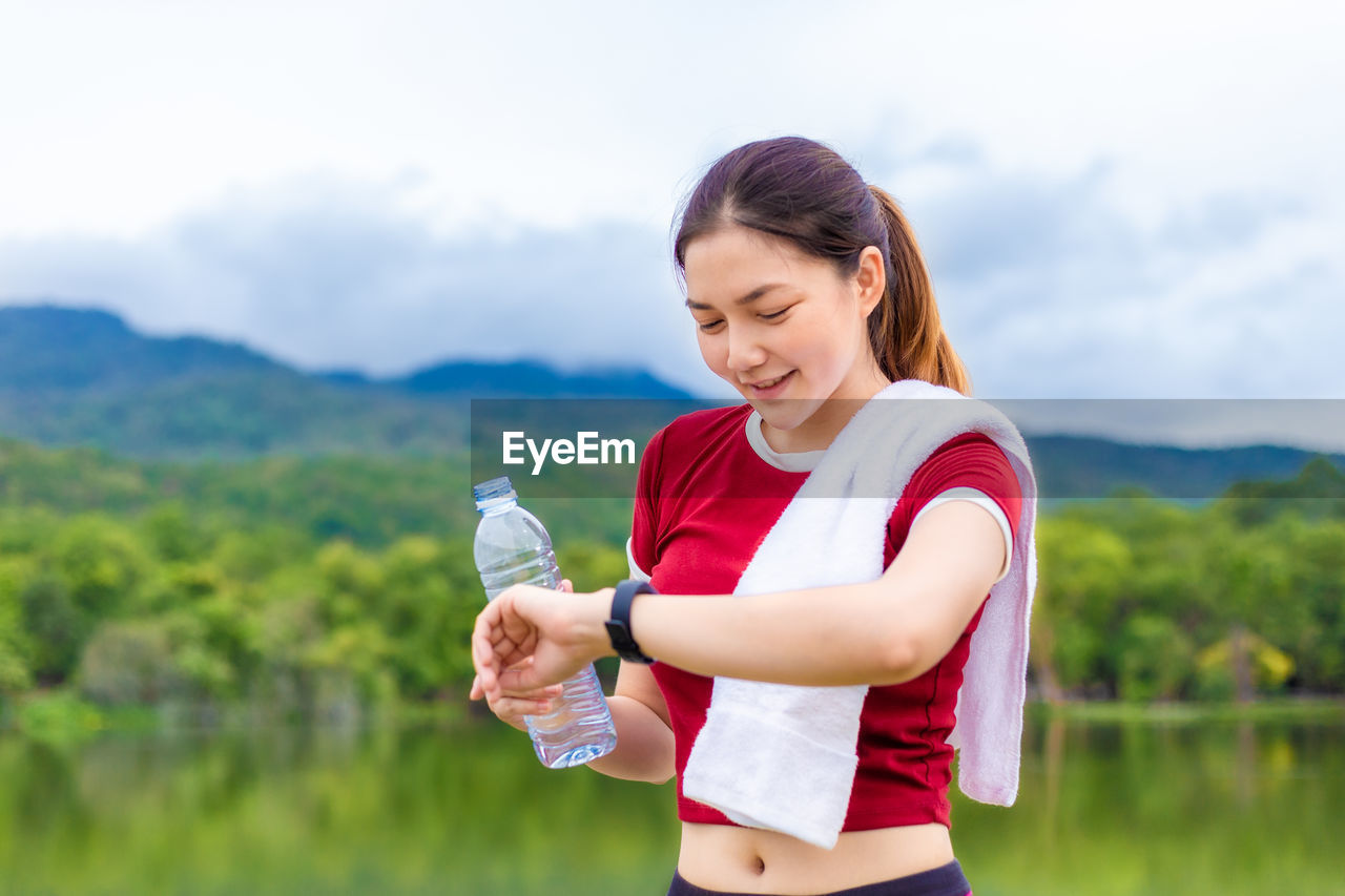 SMILING WOMAN STANDING AGAINST SKY