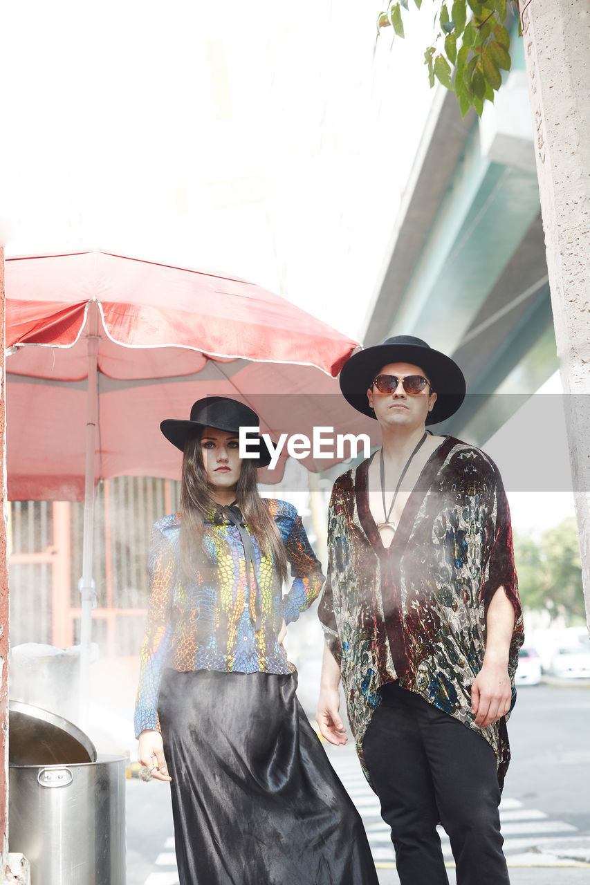 Confident stylish couple in hipster clothes standing on street in summer and looking at camera