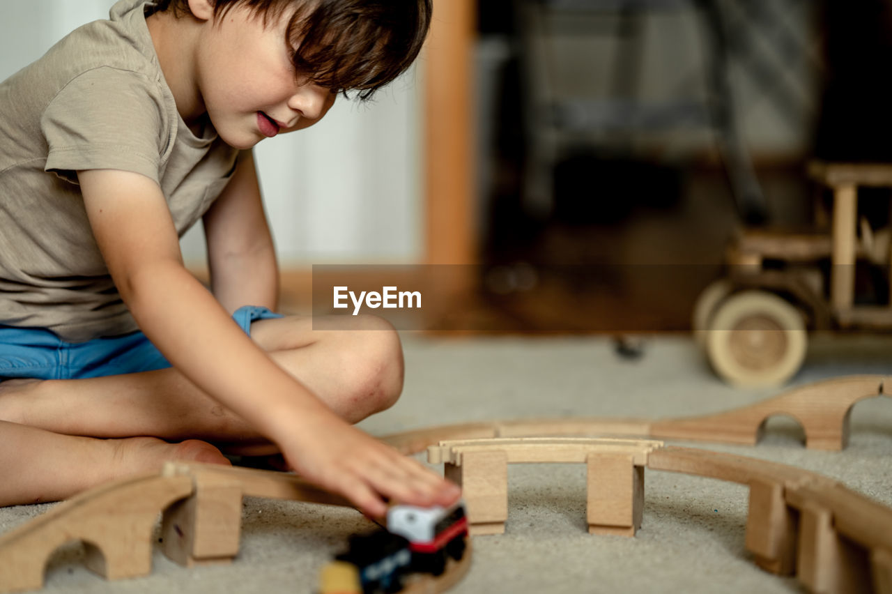 The boy is playing by train at home. the child is building a railway from a wooden construction set