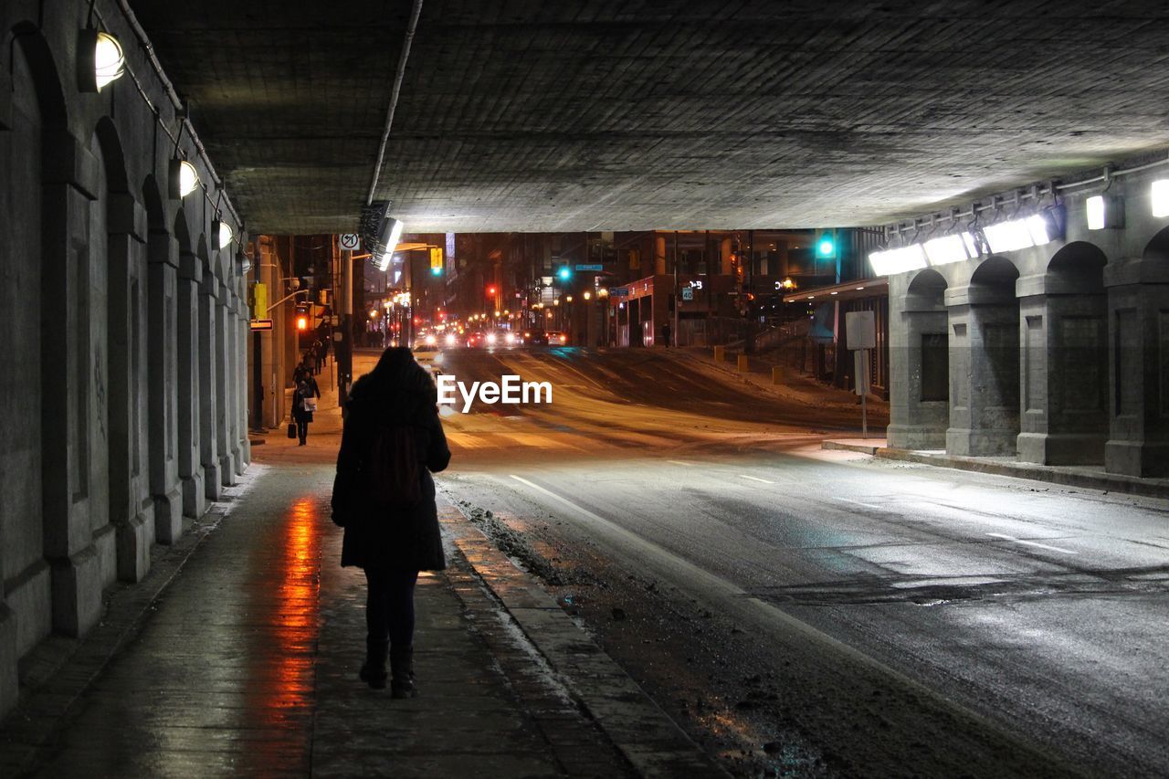 Rear view of woman walking on road at night