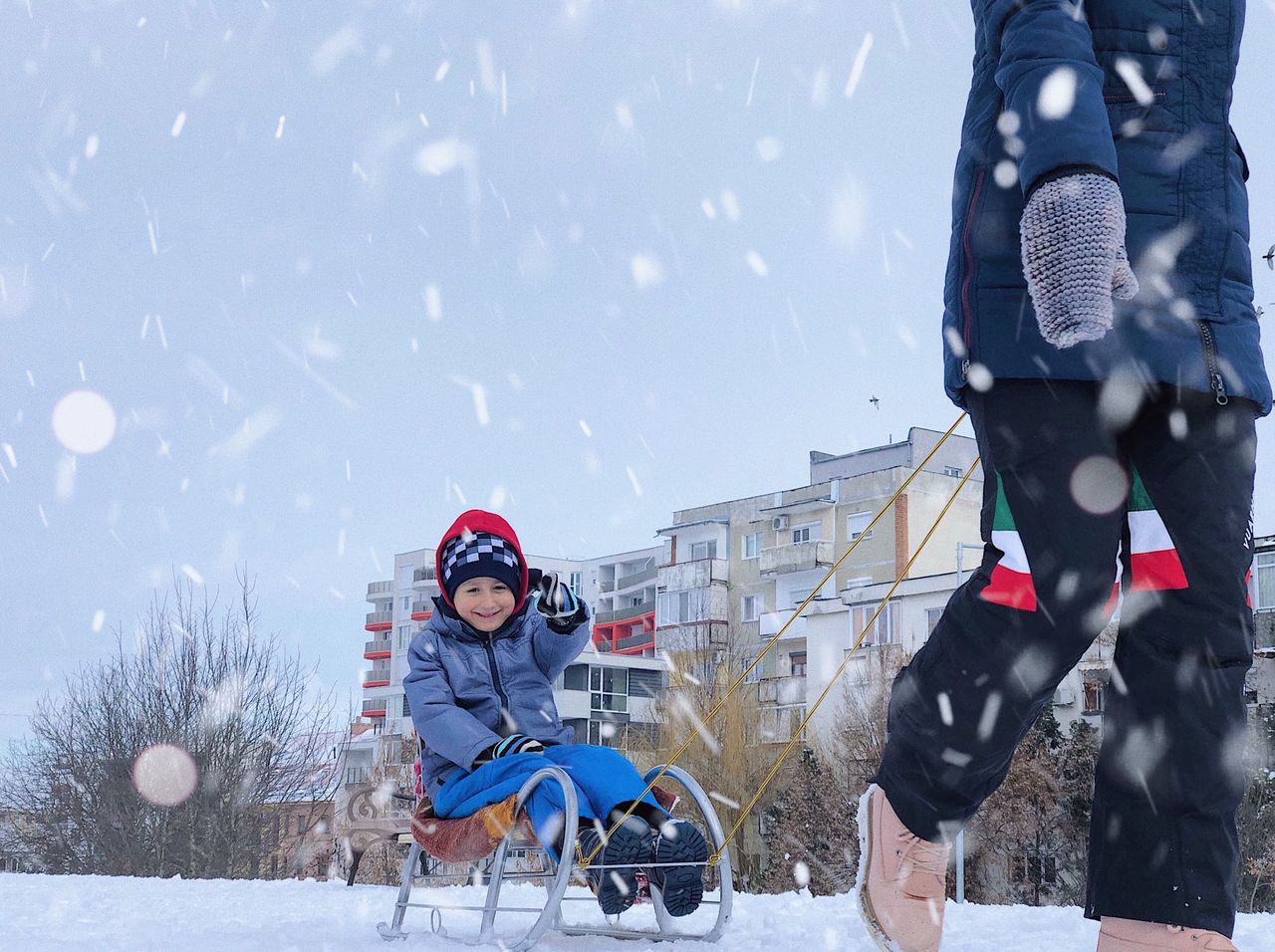 Low section of parent pulling sled with son on field during snowfall