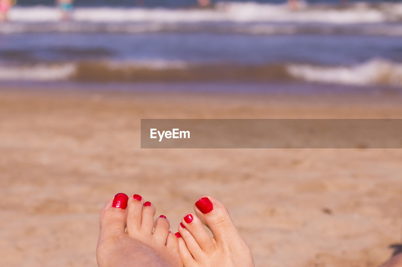 Low section of woman with red nail polish at beach