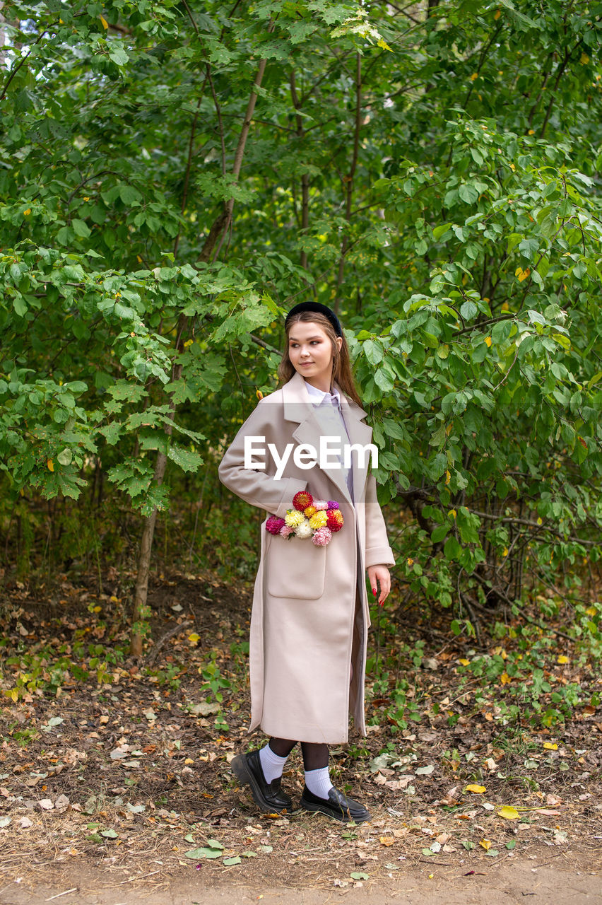 one person, full length, plant, women, adult, standing, nature, green, young adult, tree, portrait, clothing, smiling, front view, looking at camera, forest, lifestyles, traditional clothing, happiness, female, outdoors, growth, holding, day, costume, emotion, robe, person, leisure activity, dress, woodland, kimono, land, looking