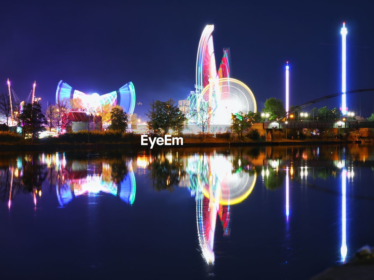 ILLUMINATED BUILDINGS BY RIVER AGAINST SKY