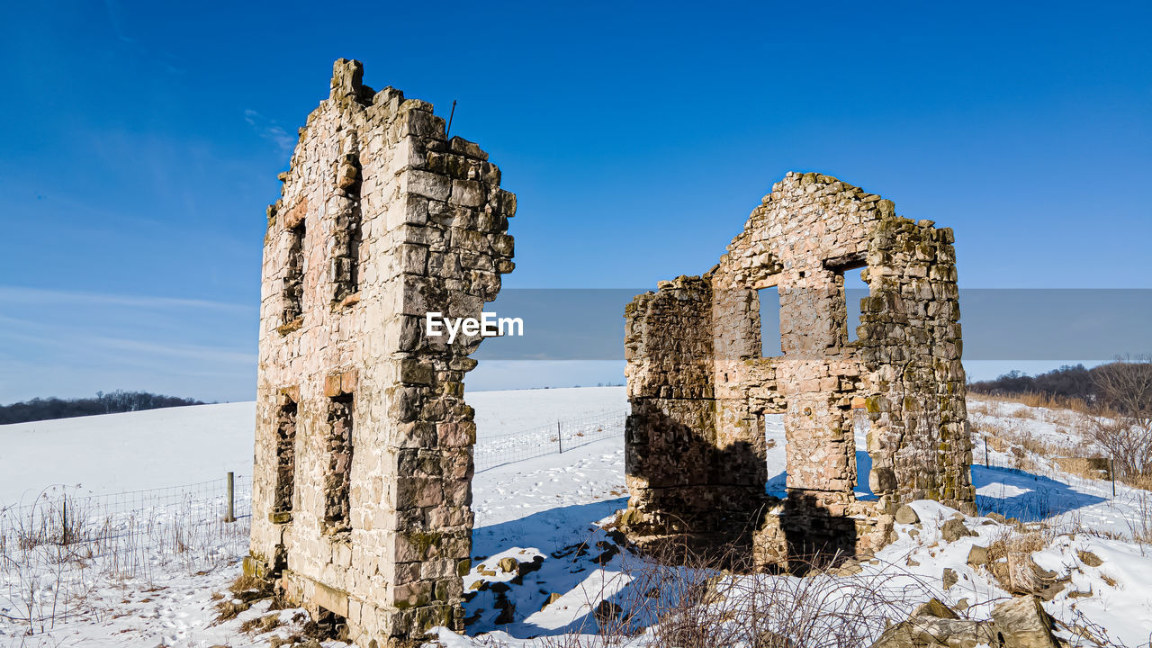 sky, winter, snow, nature, history, scenics - nature, blue, travel destinations, cold temperature, architecture, the past, landscape, mountain, land, clear sky, no people, travel, old ruin, rock, environment, ruins, day, ancient, beauty in nature, outdoors, tranquility, sunny, built structure, plant, old, sunlight, tourism, tranquil scene, mountain range, tree, building, non-urban scene