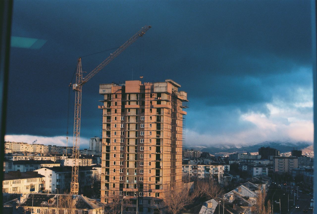 Building and crane against cloudy sky in city