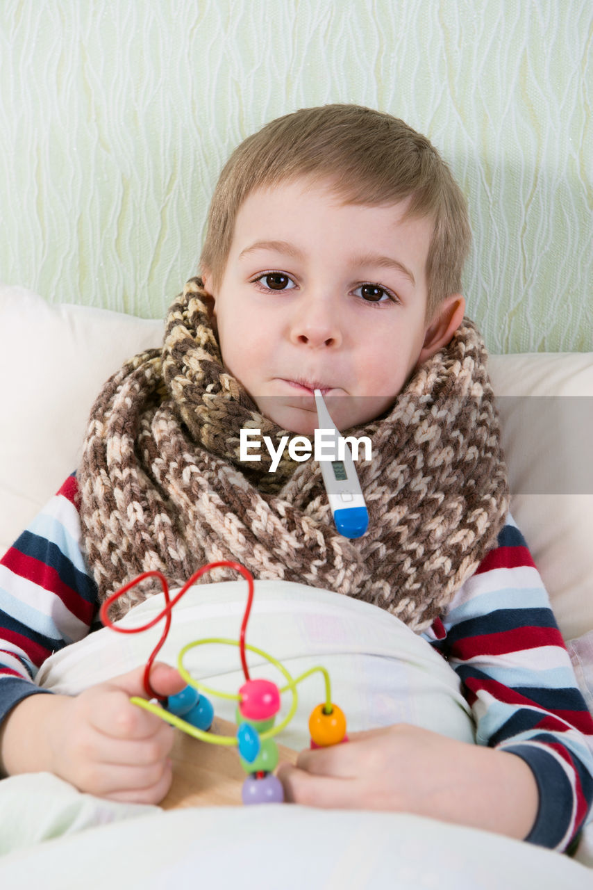 Portrait of cute boy with thermometer relaxing on bed at home