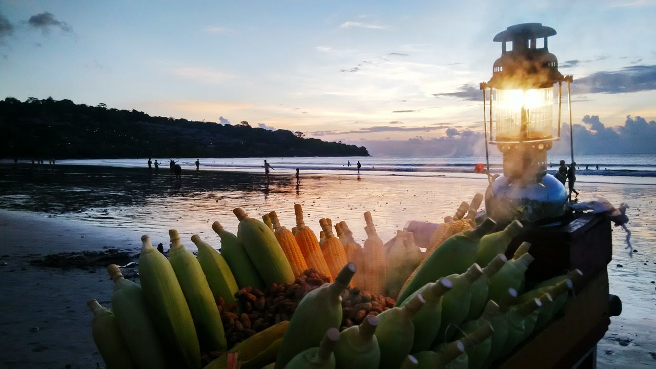 Illuminated oil lamp on sweetcorn at beach against sky during sunset