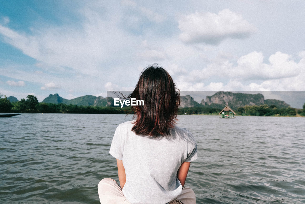 Woman sitting on wooden raft over lake against sky