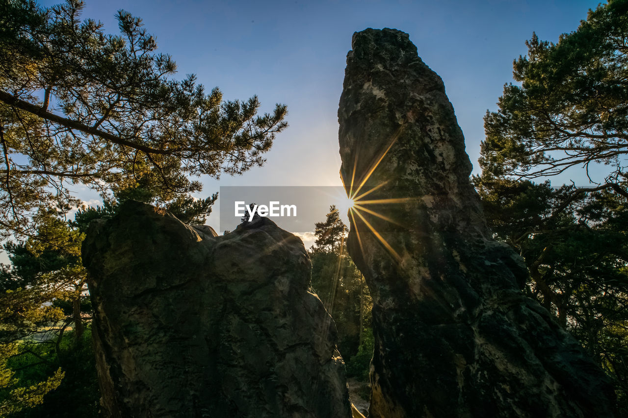 Low angle view of sunlight streaming through rocks against clear sky