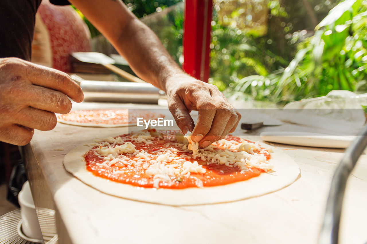 Adding grated cheese to unbaked pizza on wooden table, top view