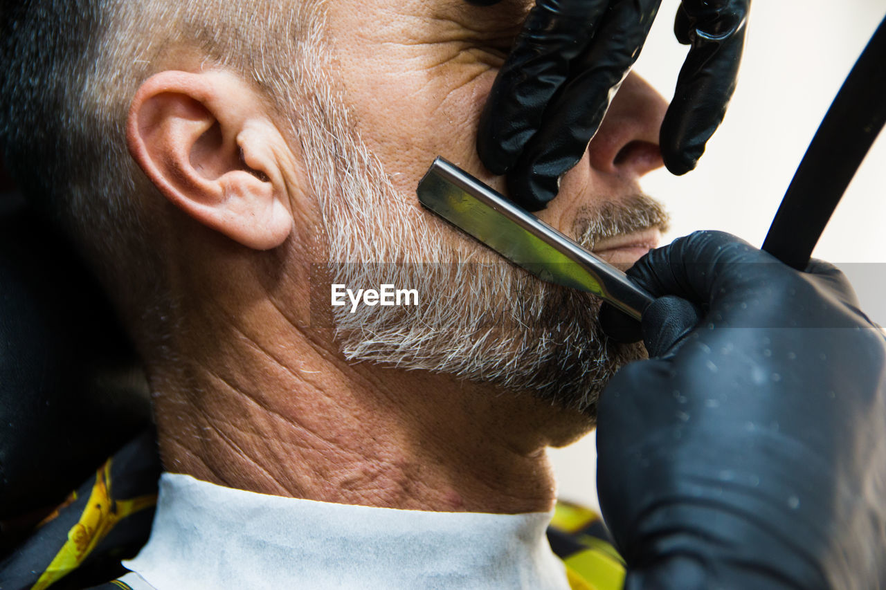 Cropped hands of barber cutting beard of man at salon