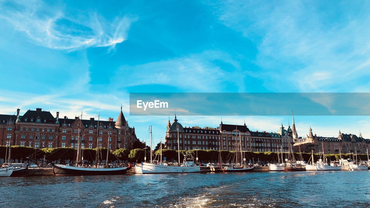 Sailboats in river by buildings against sky