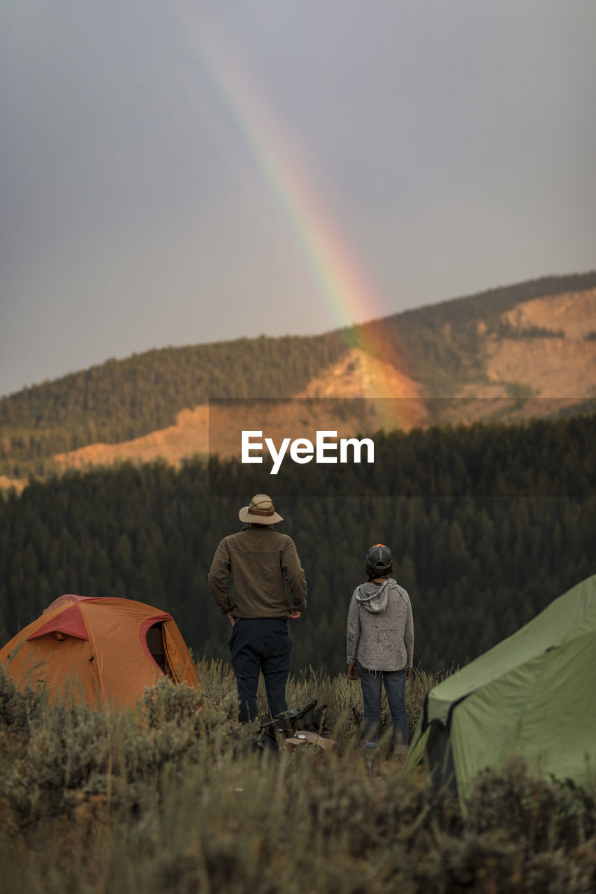 Rear view of couple camping on mountain against sky during sunset