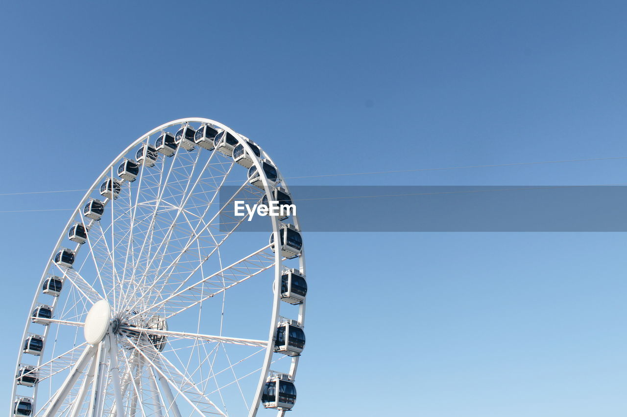 Low angle view of ferris wheel against clear blue sky