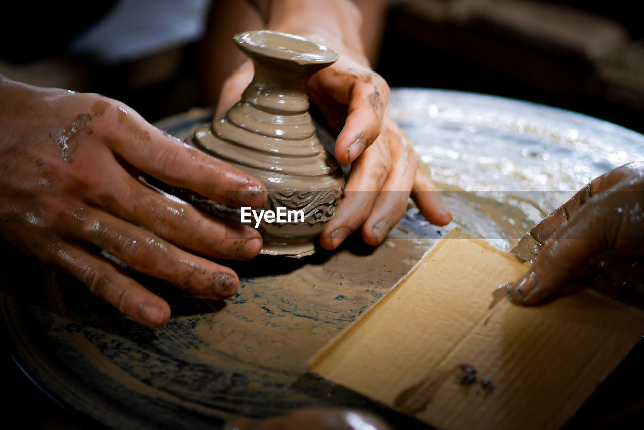 Cropped hands of people working on pottery wheel