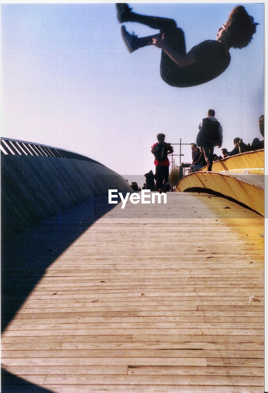 Young man jumping on footpath against sky