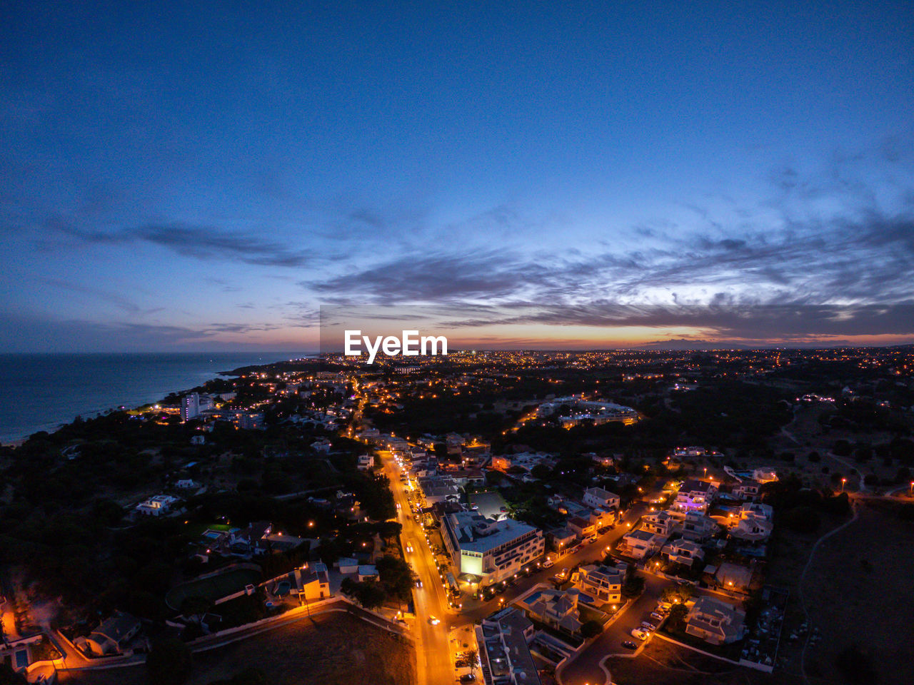 HIGH ANGLE VIEW OF ILLUMINATED BUILDINGS AGAINST SKY AT DUSK