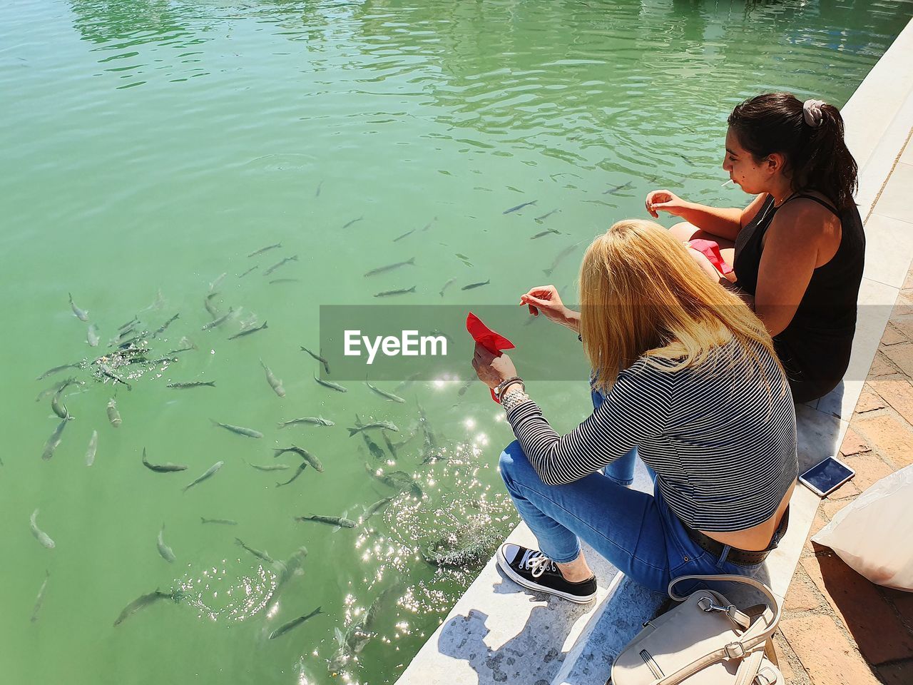 High angle view of friends feeding fish in lake