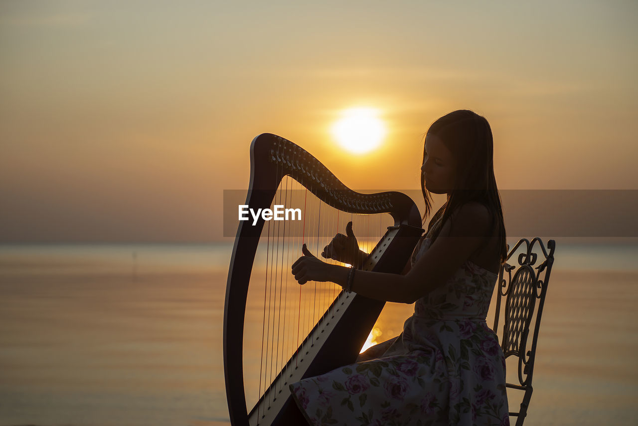 Woman playing musical instrument at beach during sunset