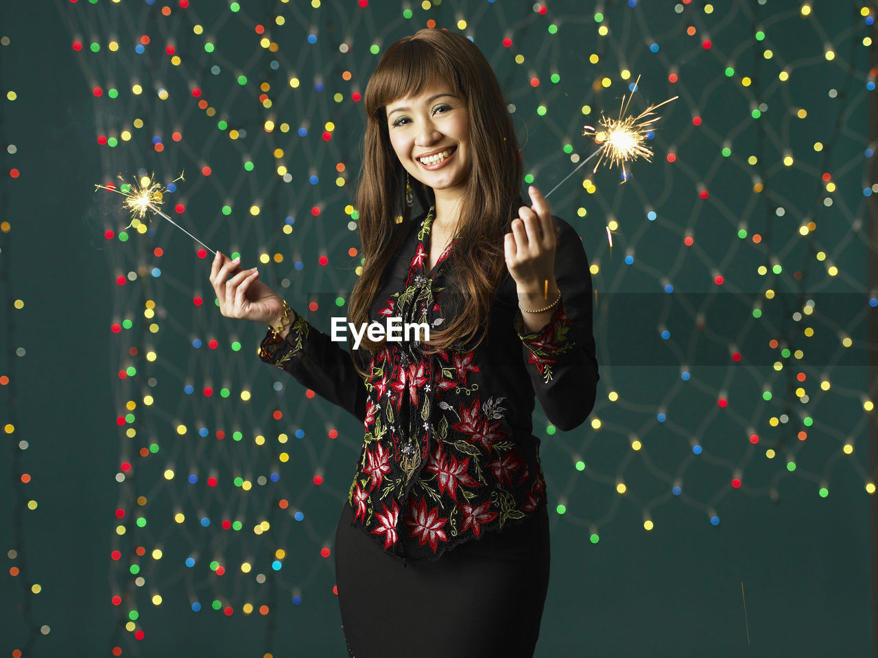 Portrait of woman with burning sparklers against illuminated lights