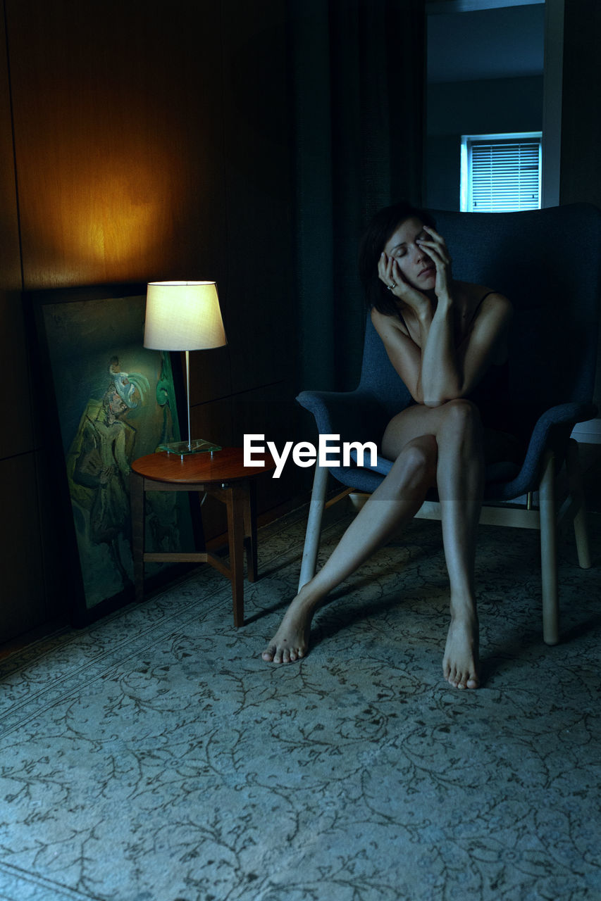 YOUNG WOMAN SITTING ON CHAIR IN HOME