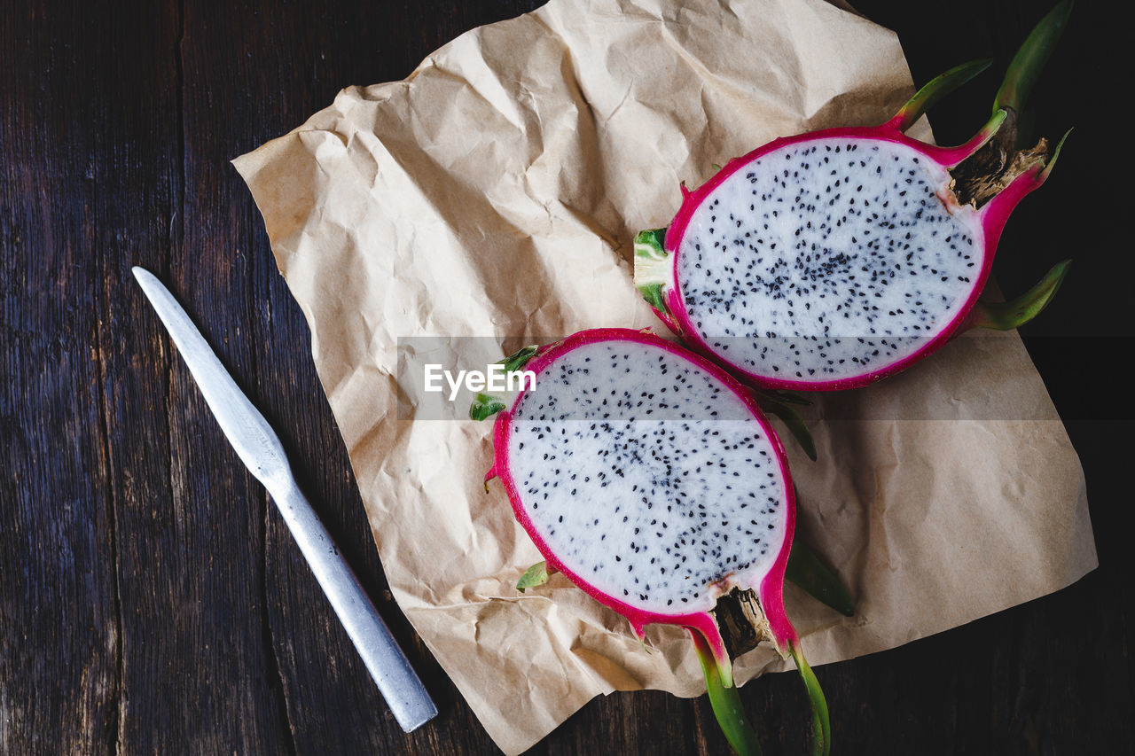 High angle view of pitaya with knife and paper on wooden table