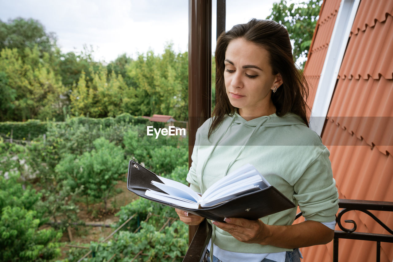 Young woman stands on the balcony with notepad in hand