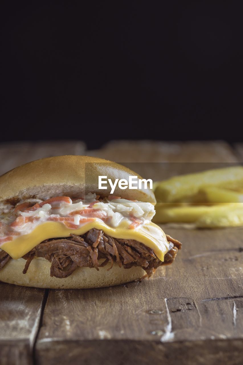 Close-up of burger on wooden table against black background