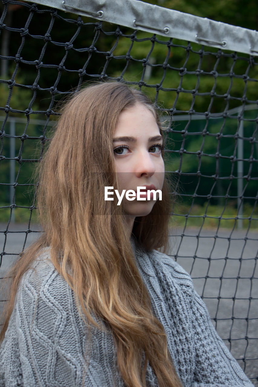 Close-up portrait of young woman against net