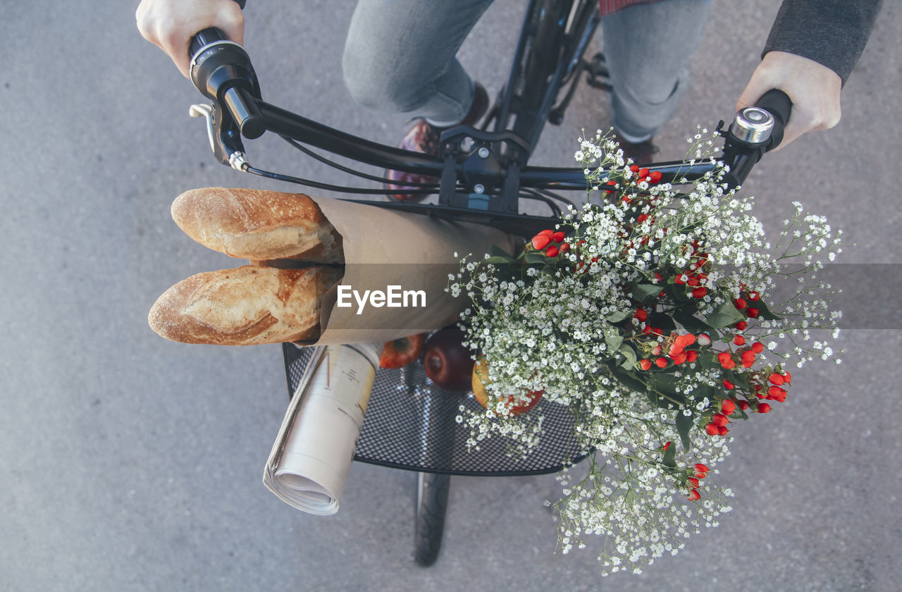 Man with apples, bouquet of flowers, newspaper and baguettes in bicycle basket