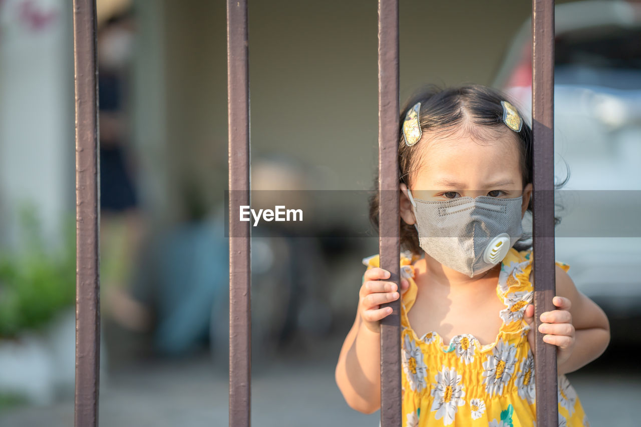 Girl standing at fence wearing medical face mask to prevent flu, pollution and covid 19.