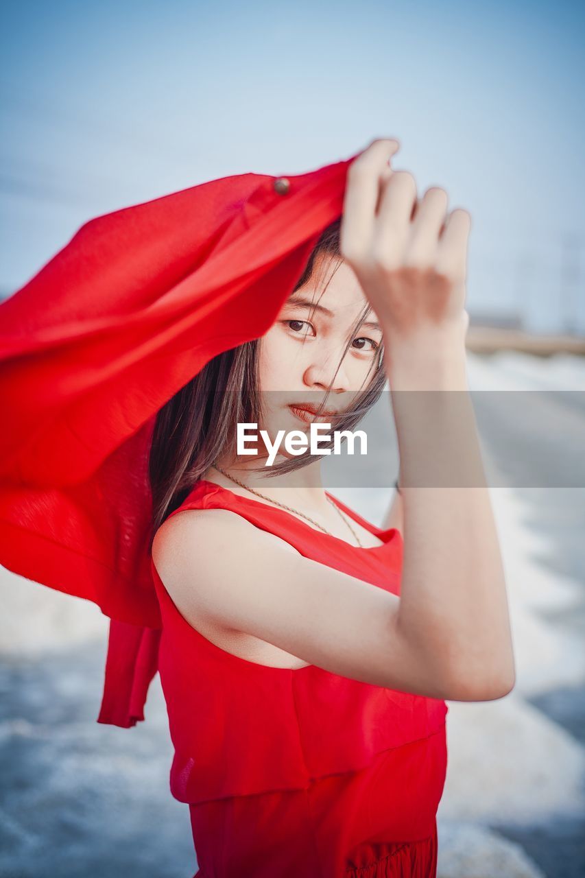 A beautiful woman in a long red dress stands tall among salt fields and blue skies.