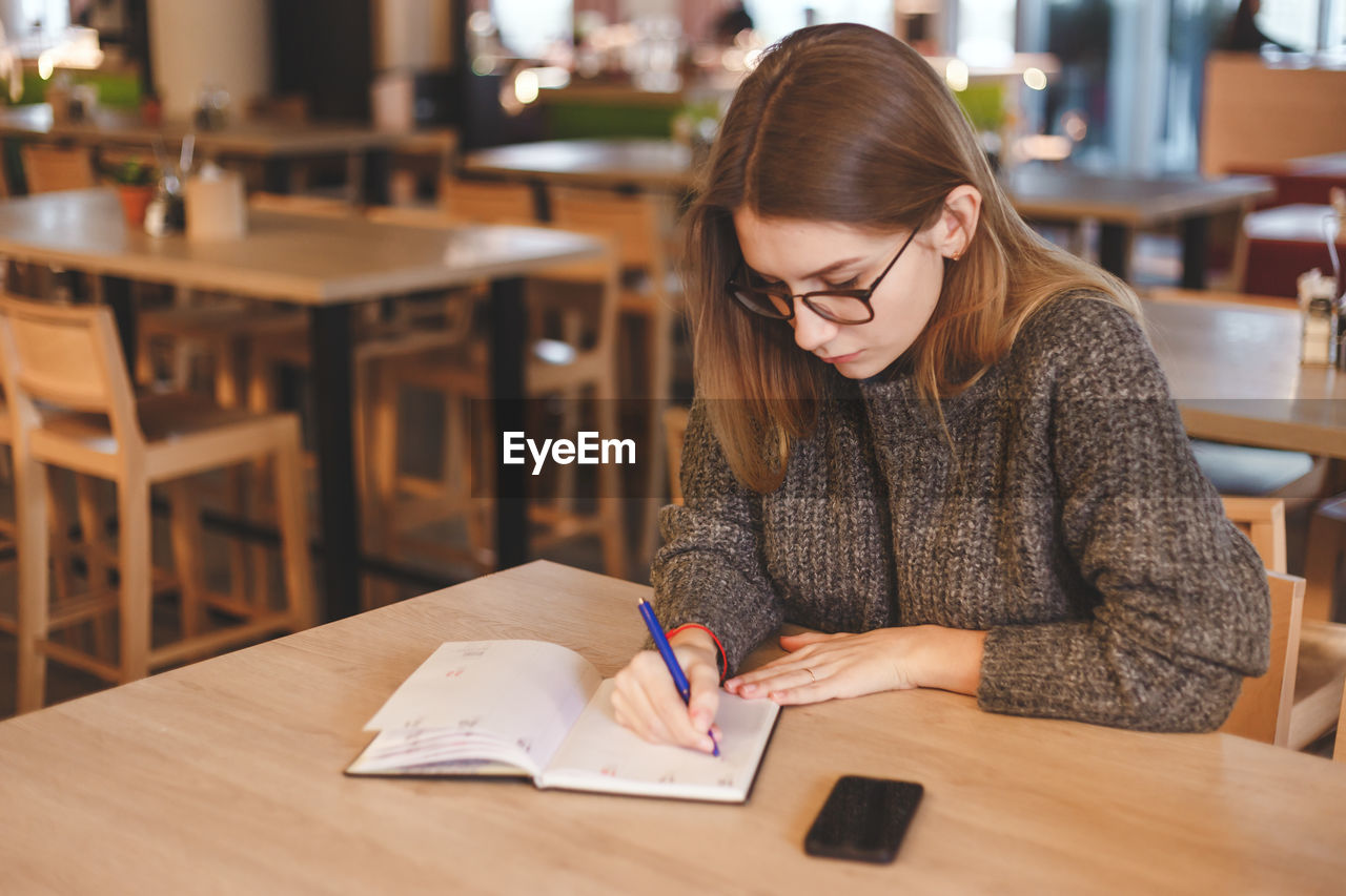 YOUNG WOMAN SITTING ON TABLE WITH BOOK