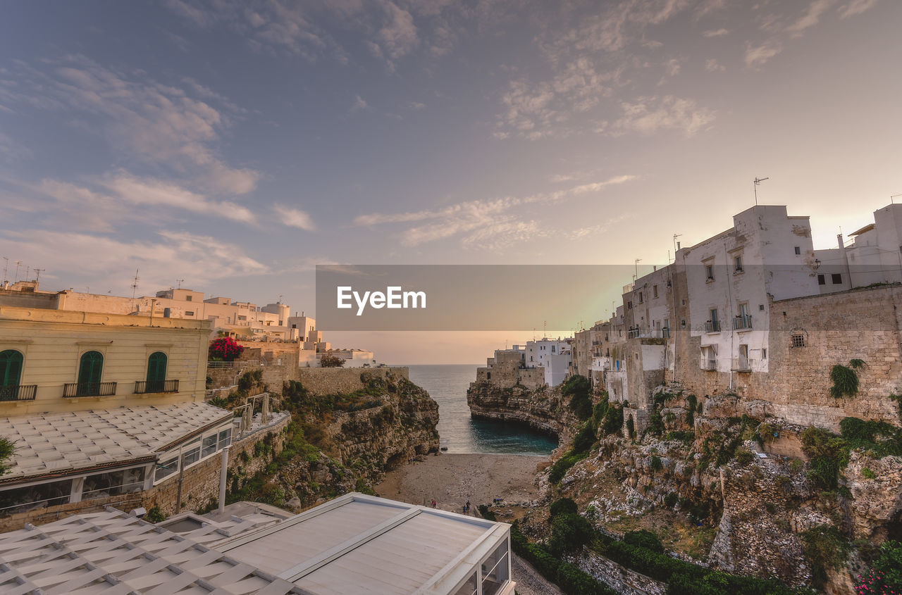 Buildings in town by sea against sky during sunset