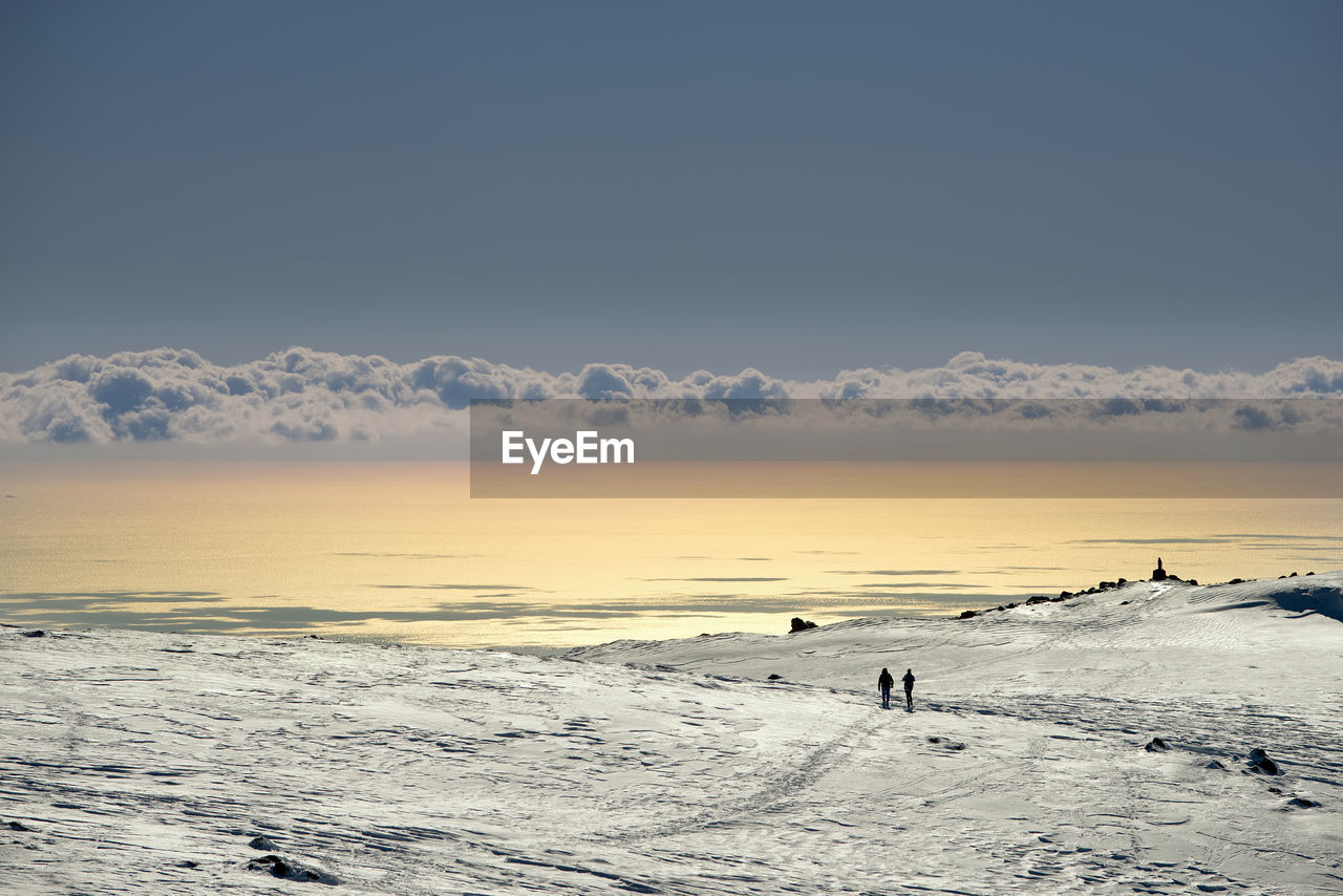 People on snow covered landscape against golden sea