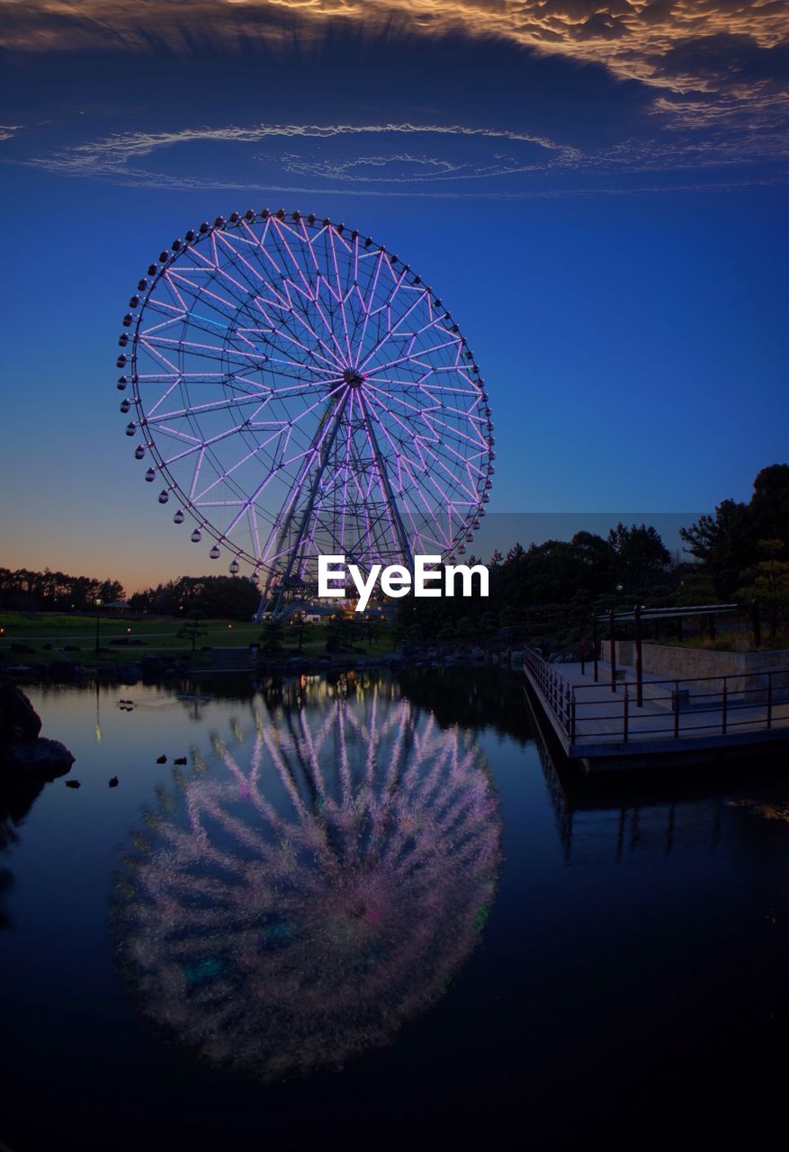 Ferris wheel by lake against clear blue sky at night