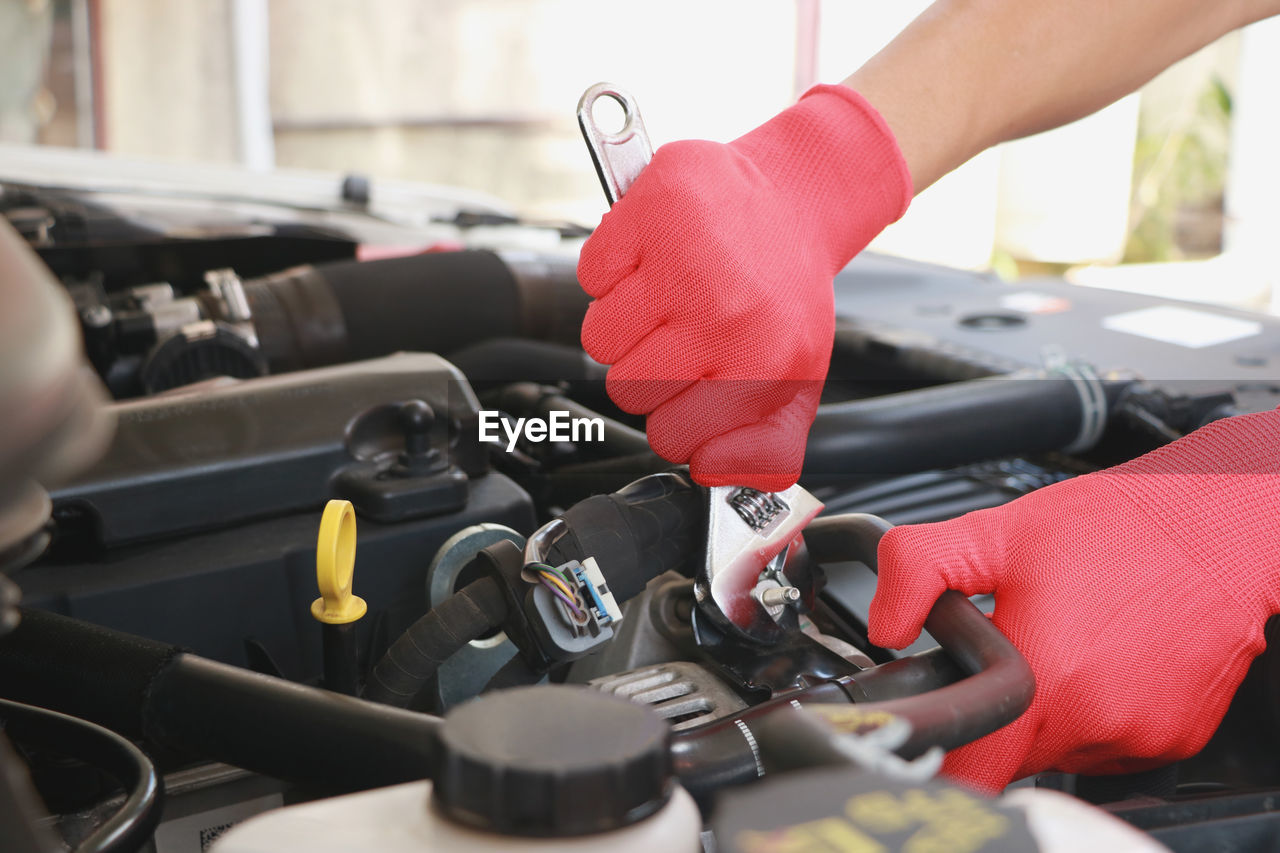 Cropped hands of mechanic holding wrench and repairing car engine